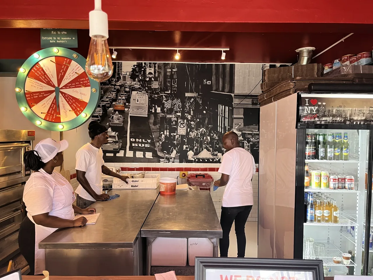 An NY Slice crew prepping at the steel counter under the New York street mural