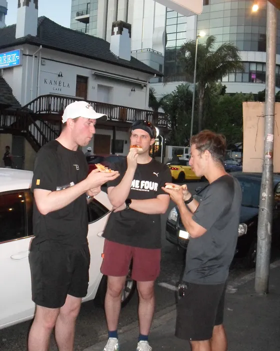 Three runners eating slices in the street