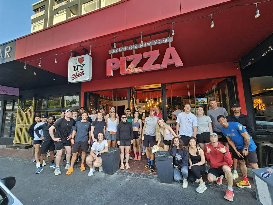 A run club group outside a NY Slice store