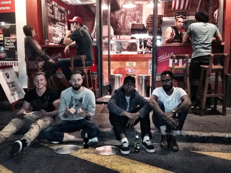 Friends sitting outside a NY Slice store at night